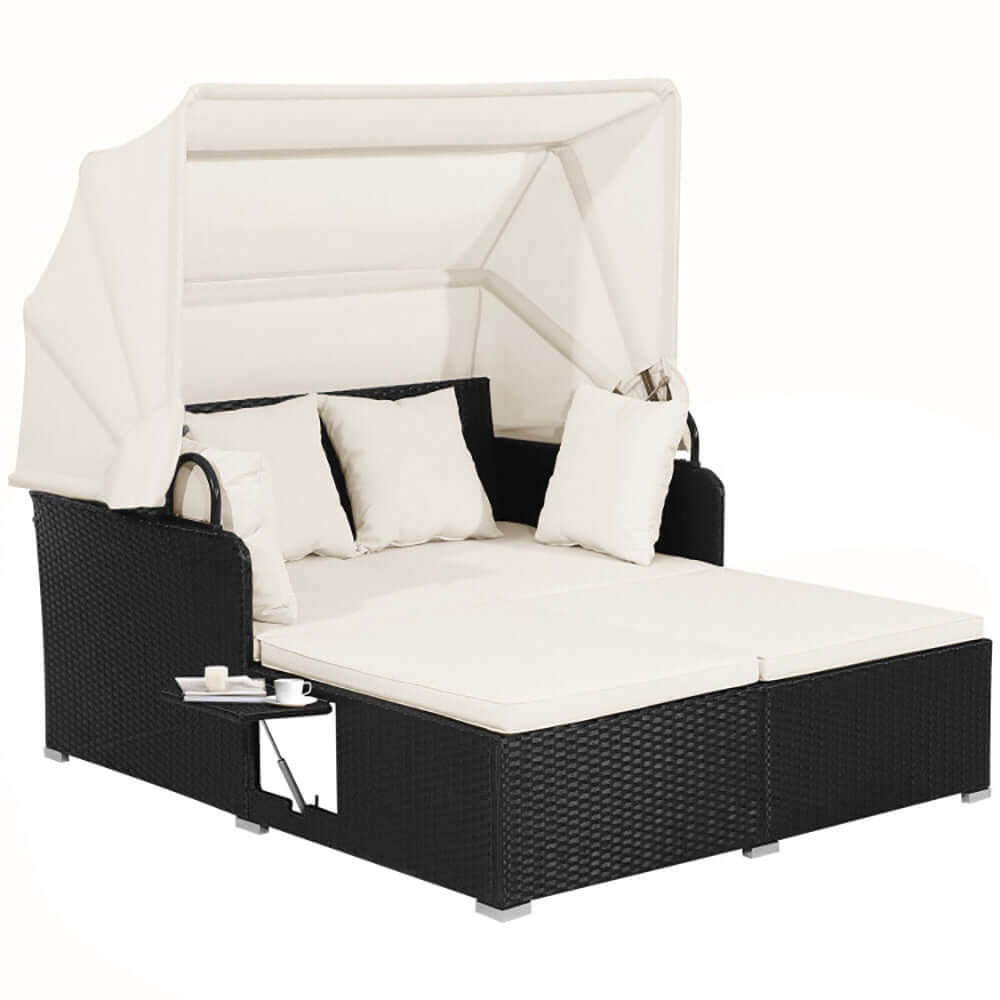 Patio rattan daybed with retractable canopy, cream cushions, and side table for outdoor relaxation.
