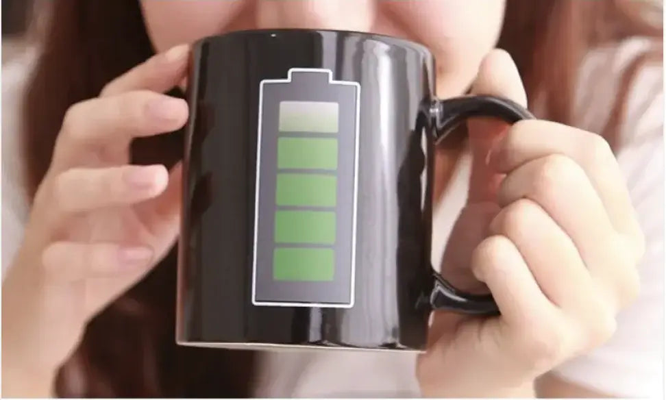 Person holding a black ceramic coffee mug with a battery graphic, perfect for coffee lovers and as a unique gift.