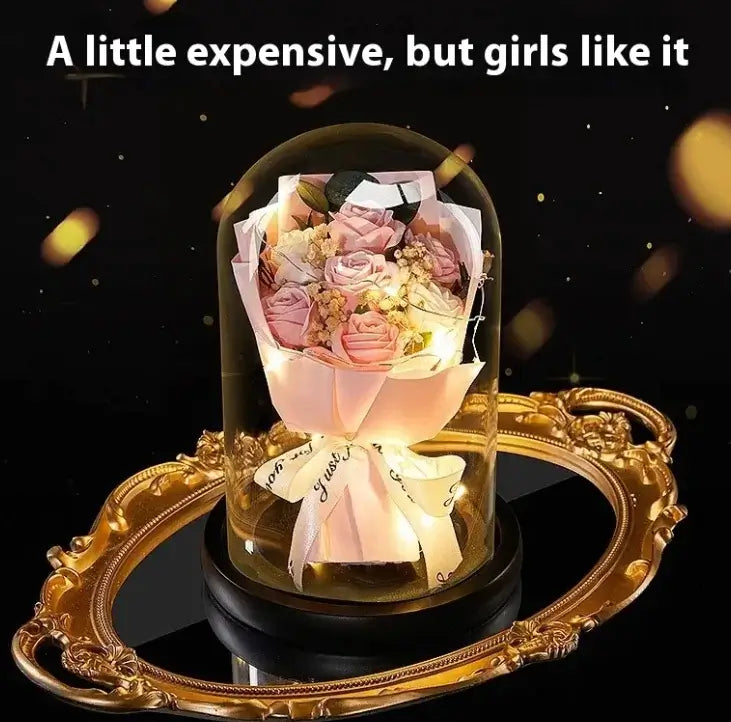 Elegant lighted display of preserved roses and flowers in a glass dome, set on a decorative gold tray.