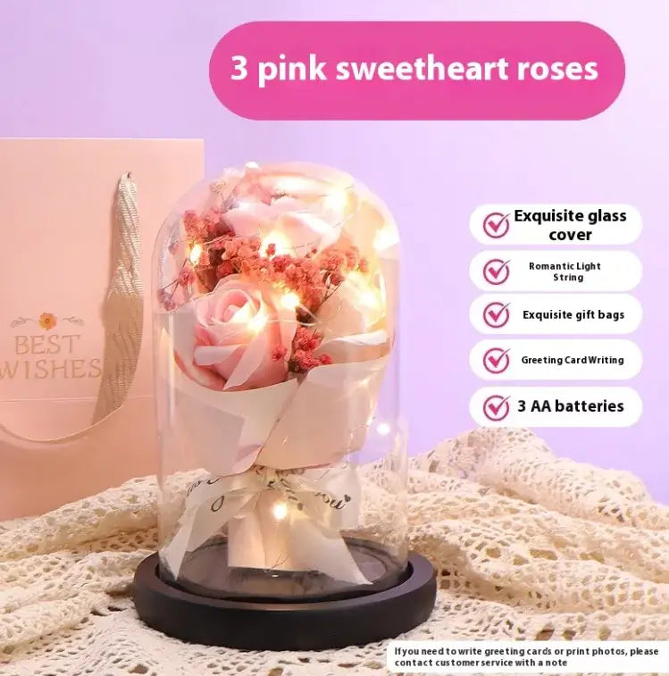 Three pink sweetheart roses in a glass dome with soft lighting and decorative details for an elegant display.