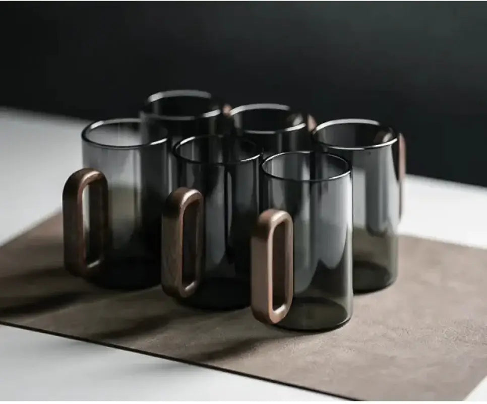 Set of six smoky gray borosilicate beverage cups with wooden handles on a minimalist background.