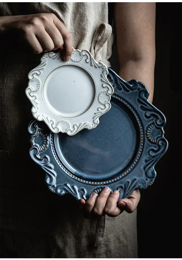 Elegant Baroque dining plates in white and blue held by a person, showcasing intricate designs and unique shapes.