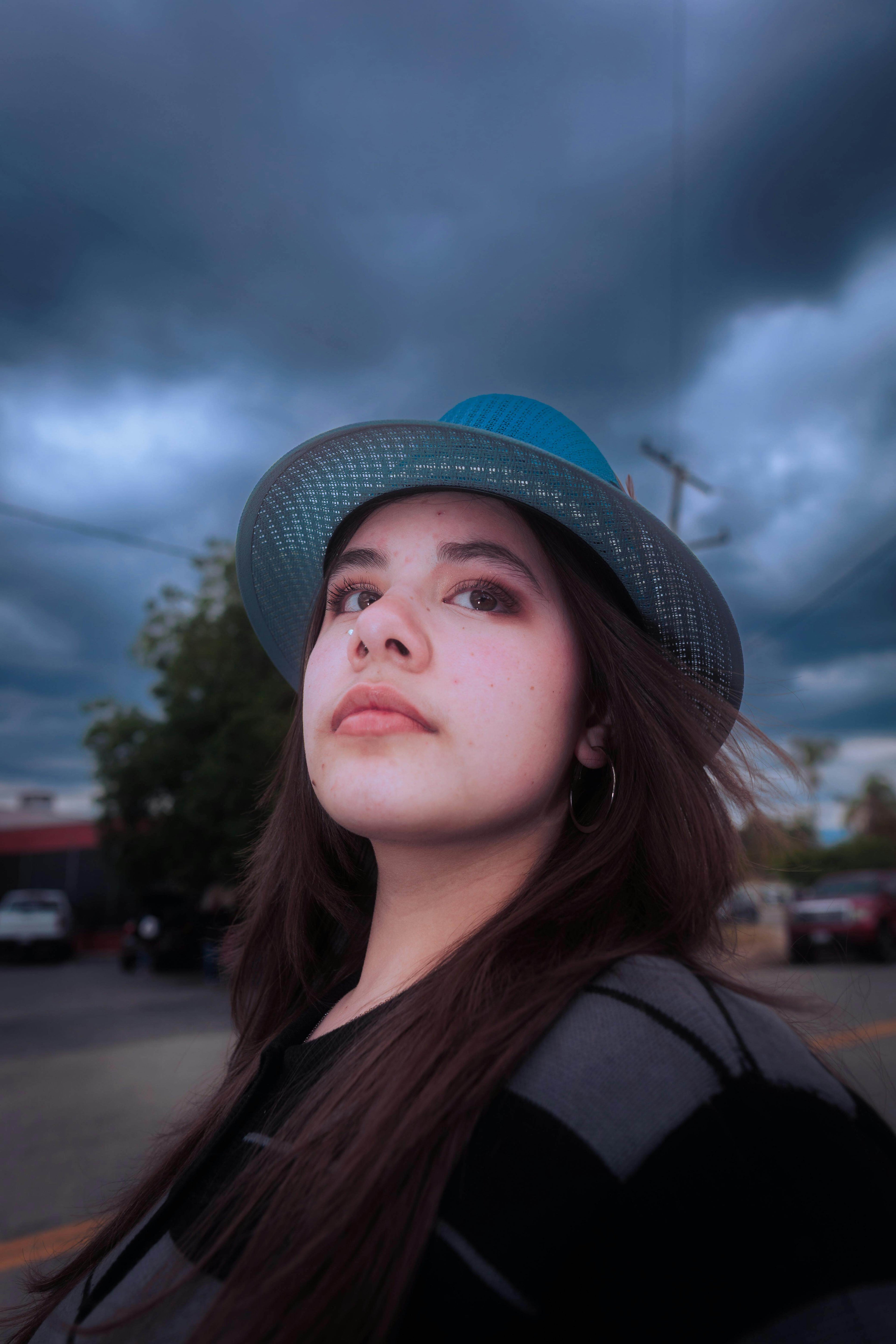 Young woman wearing a blue hat gazing upward with dramatic cloudy sky in the background.
