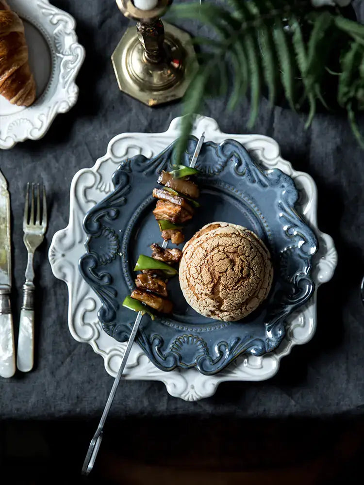 Elegant Baroque dining set featuring a blue plate with skewers and a bread roll, enhancing a sophisticated dining experience.
