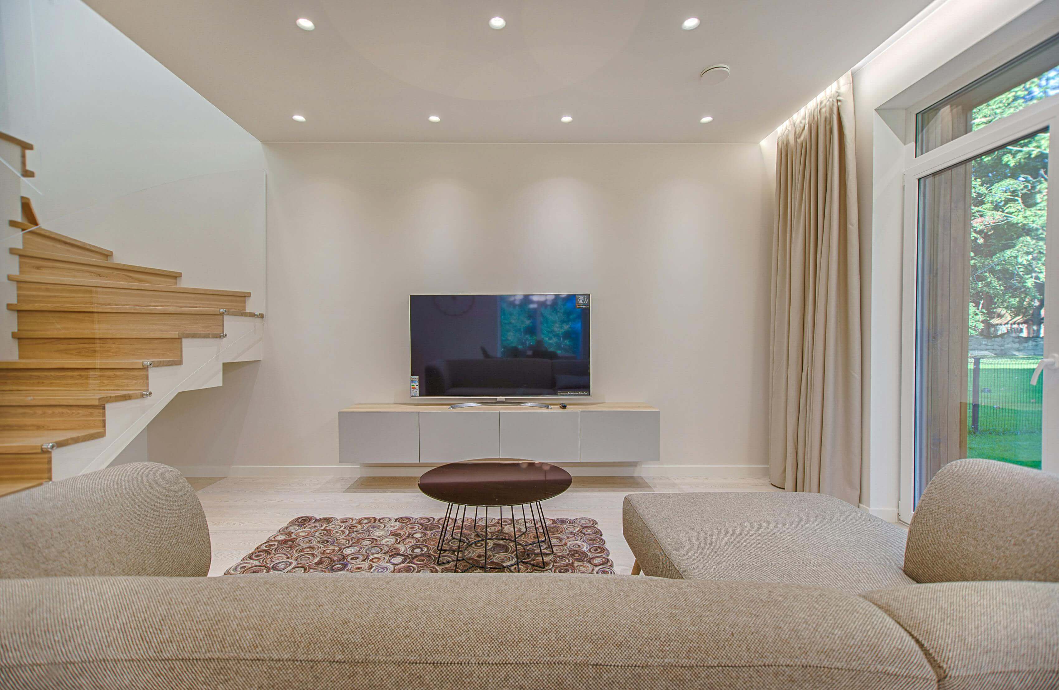 Contemporary living room with a sectional sofa, coffee table, TV unit, and large windows for natural light.