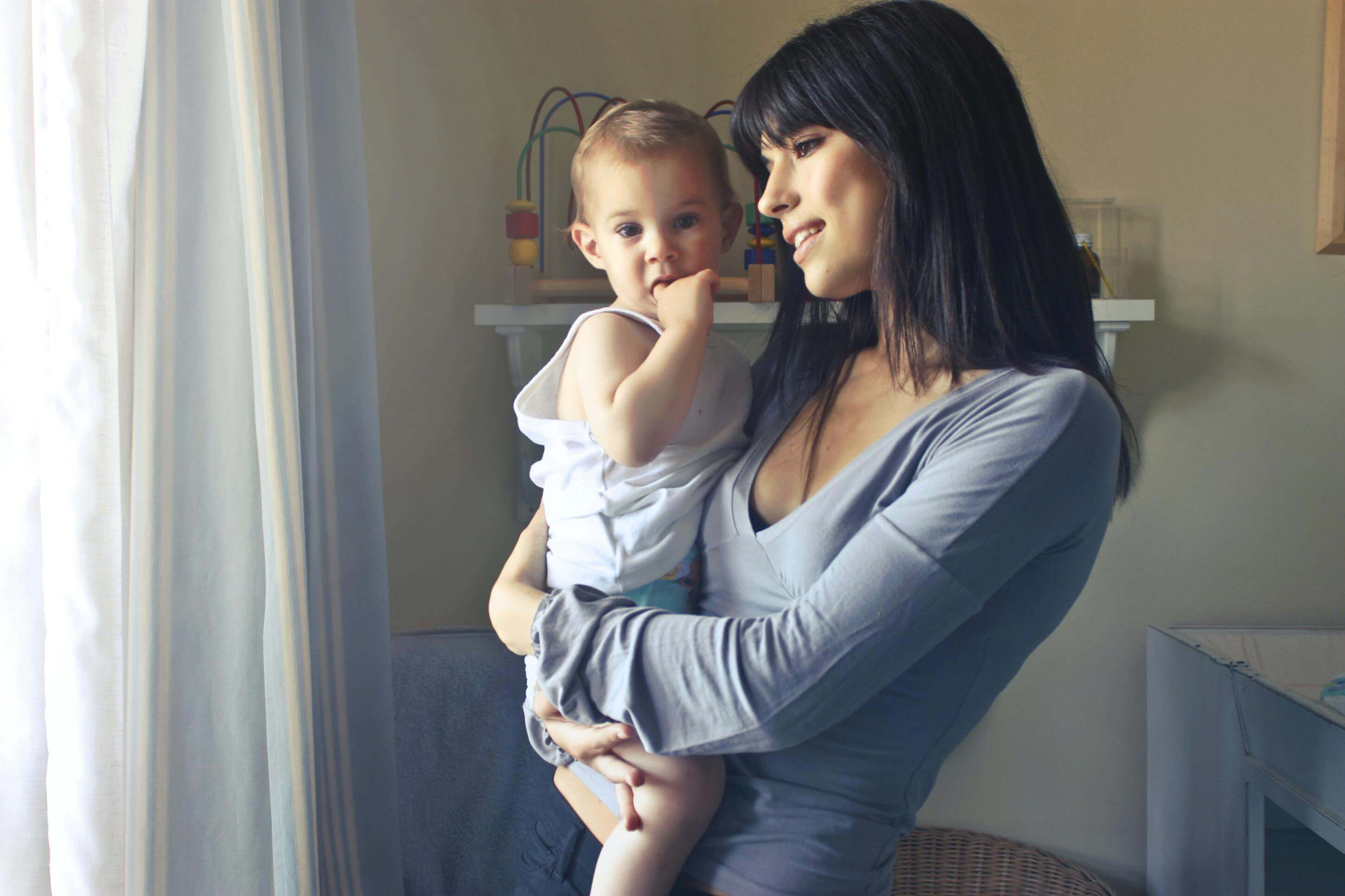 Mother holding her toddler in a cozy, sunlit room, showcasing a warm and loving moment.
