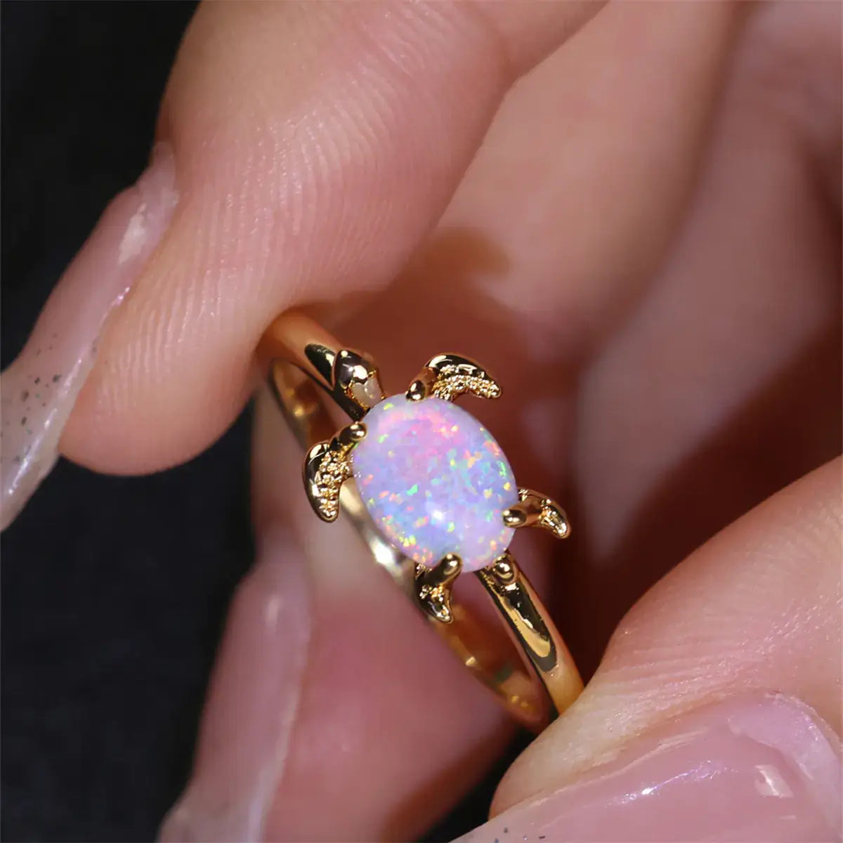 Round white opal turtle ring featuring a gold band, elegantly held between fingers, showcasing its charm.